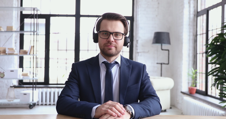 Confident male support service representative wears suit and tie talking to web camera. Businessman in headset communicates by conference video call. Helpline manager speaking to customer, webcam view Royalty-Free Stock Footage #1048319119