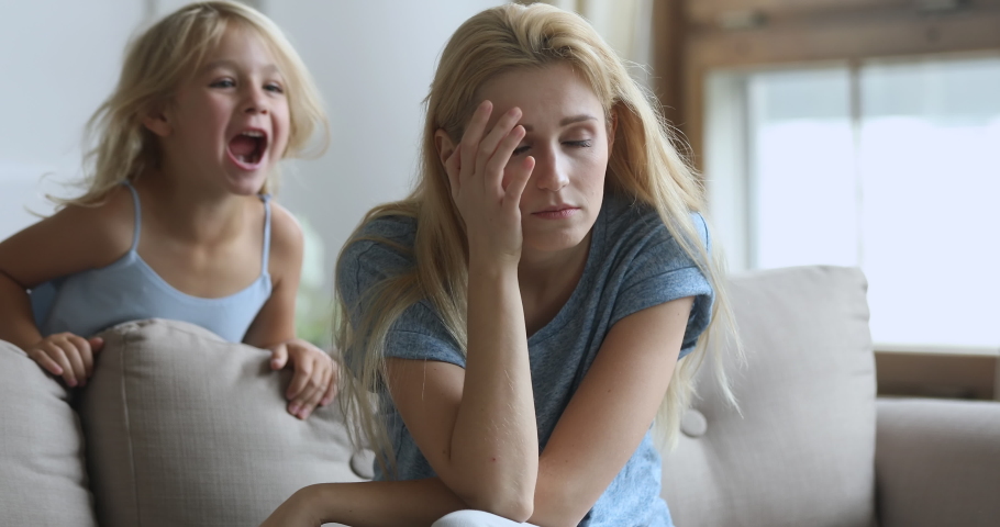 Tired young woman irritated by bad daughter behavior. Active little preschool girl shouting grabbing moms hair. Exhausted mother holding head, suffering from strong headache, annoyed by loud child. | Shutterstock HD Video #1048329337