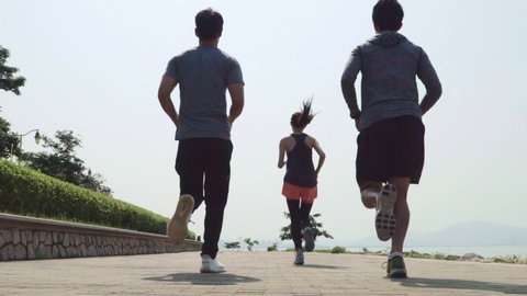 rear view of a group of five young asian adults running by the sea in slow motion