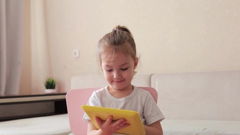 Four years little girl with pretty face girl using childrens digital tablet technology device sitting on chair near sofa.