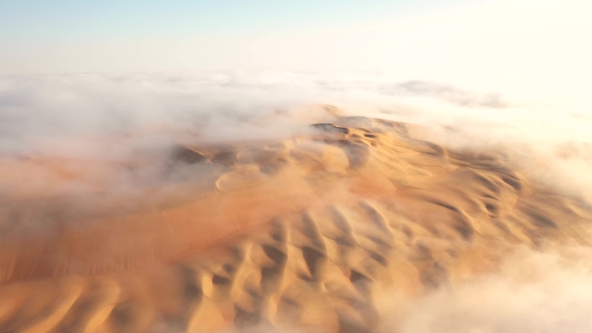 Aerial view of a drone flying over massive sand dunes covered by thick fog clouds at sunrise. Liwa desert, Abu Dhabi, United Arab Emirates. Royalty-Free Stock Footage #1048349584