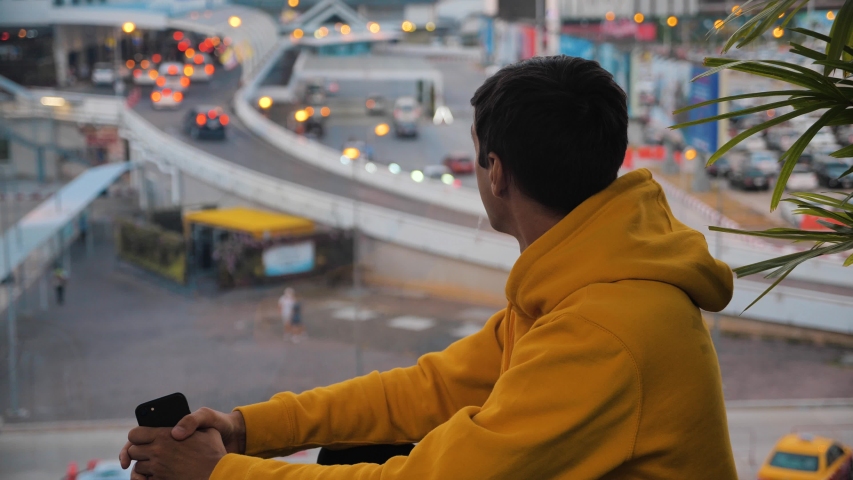 Young man tourist looking out of a large window at the city