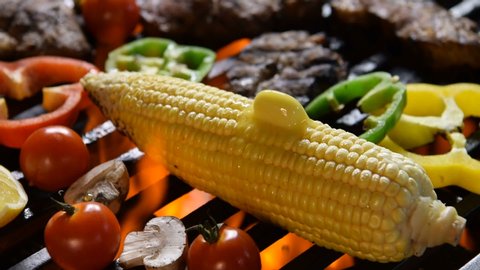 Corn with melting butter on the flaming grill .