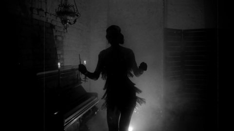 Old film style grain added. black and white color dark mysterious female silhouette. mouthpiece in hand. short sexy vintage dress 20s. retro young beautiful woman dances. backdrop room piano smoke