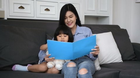 Family concept. Mother and daughter are reading books together in the living room. 4k Resolution.