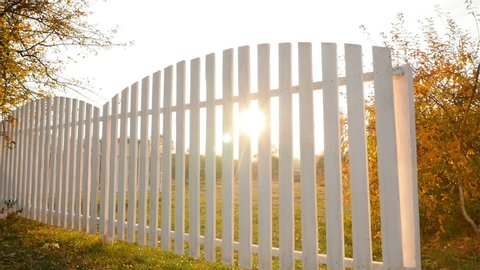 Beautiful white fence with a green lawn. Bright rays of the sun. Camera in motion