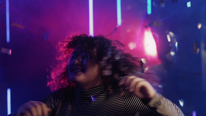 Neon girl. Fun celebration. Happy young woman with curly hair enjoying confetti rain in blue lights.