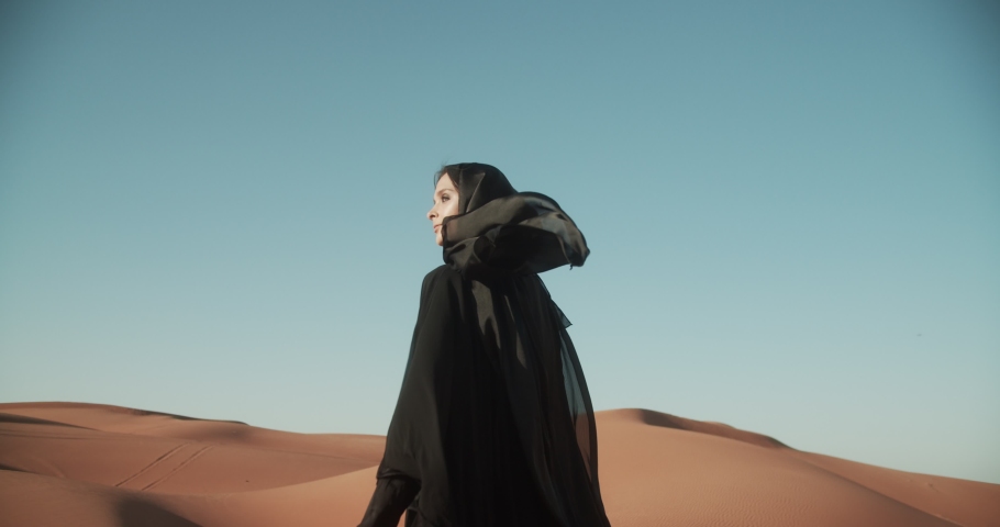Young beautiful girl in traditional Abaya dress walks along the dunes in the desert of Dubai. 4K Slow Motion