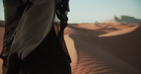 Close-up of girl in traditional Abaya dress walking barefoot along the dunes in the desert of Dubai. 4K Slow Motion