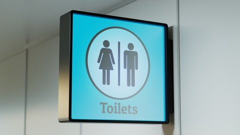 A camera is focuses on sign of toilets in public place like airport terminal, hospital, bus or train station and any other type. Blue background. Entrance. Sunny day. Indoor. Corridor. Guide. Access
