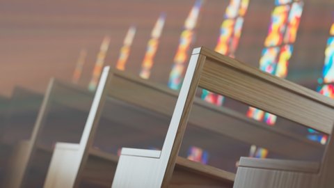 Endless rows of wooden church benches lit by the sun through a stained glass window. Empty chapel. Colourful god rays giving religious, spiritual meaning. Seamless looping animation.
