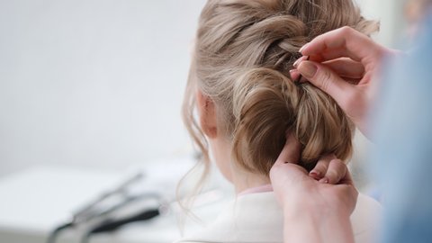 Close up female hairdresser hands fixing plaiting hairstyle using barrette back view. Woman blonde model during finishing braid use hairpin. 4k Dragon RED camera