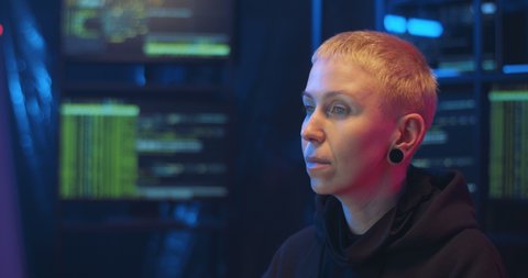 Portrait of Caucasian woman hacker with short hair sitting at night in front of computer. Cyber policewoman turning face to camera and biting cookie. Close up female eating sweets in monitoring room.