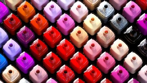 Seamless looping animation with many opened nail polish bottles arranged by shade. Top diagonal view of vibrant, beautiful, timeless fashion colors. Elegant glass bottles on the dark surface.
