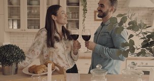 Beautiful couple, Young man and woman drinking wine and talking in kitchen. Loving people spending time together at home. 4K slow motion video.
