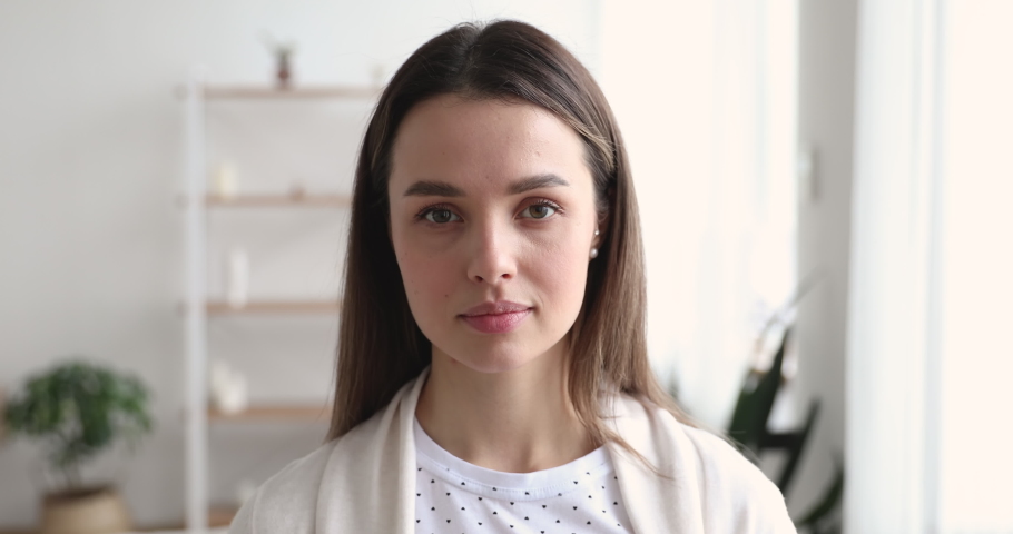 Beautiful healthy millennial single woman looking at camera at home. Happy young adult girl with attractive face standing in apartment. Smiling confident casual model posing indoors, close up portrait Royalty-Free Stock Footage #1048391236
