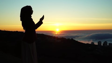 Muslim woman in a hijab are praying. The Holy month of Ramadan. Morning prayer and the beginning of fasting. Silhouette at sunrise