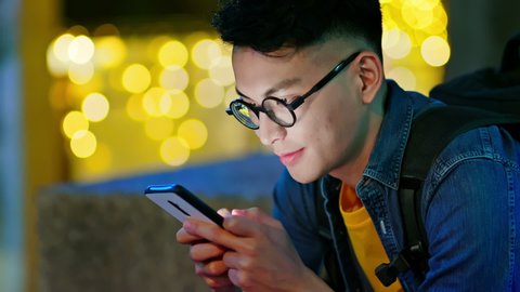 asian young man use smart phone text message outdoor in the city at night