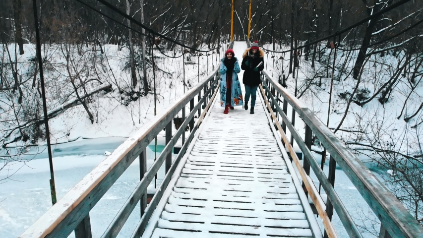 Two young women drinking hot drinks and walk on the winter bridge