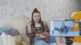 A teenage girl sitting on the couch tells something in front of the smartphone camera. The process of recording a video blog.