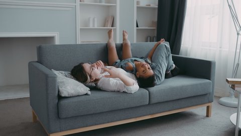 Young slim harmonic woman on sofa discuss children problem plan for day in modern apartment, concept friendly family joyful daughter girl lying on mother stomach kid active child having fun with mom