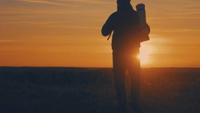 Silhouette of a man with a backpack against bright sky sunset. Sun goes down. Travel Concept. Slow video tourist go travel nature outdoors lifestyle.