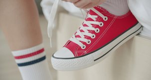 Young woman skateboarder tying shoelace in red sneakers. Close-up of legs of girl sitting on chair at home and getting ready for walking. 4k raw video footage slow motion