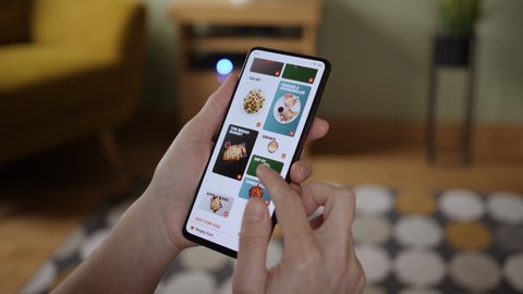 Orders Pizza Using Online Delivery. Woman Orders Food Home In Online Store Using a Smartphone. Female Ordering pizza using food delivery app. Woman at Home Lying on CouchLOS ANGELES - February 2020.