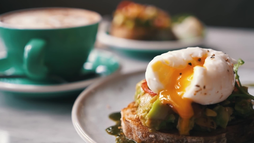 Female hands cutting poached egg avocado mashed toast, cup with coffee on background. Happy tourist girl on holidays enjoying freelance work outdoors on vacation. Tropics concept. Healthy Vegan Royalty-Free Stock Footage #1048407757