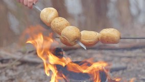 Closeup view video of two people hands cooking buns over open fire of campfire. Mother and son has fun and family adventures in cold spring or winter forest.