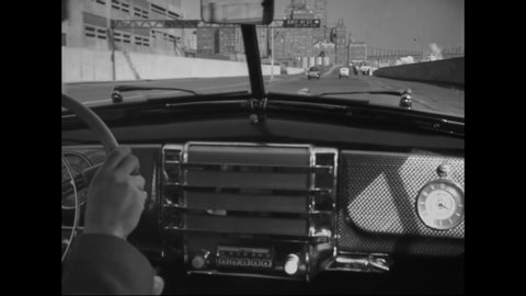 CIRCA 1940s - POV Footage is shot from the passenger seat of a car as the driver steers, changes radio stations, and drives in New York City.