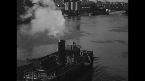 CIRCA 1930s - A tugboat moves along a New York waterway and industrial landscape with a barge.