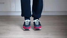 Simple jumping exercise at home  to reduce belly fat. Slow motion video clip of a man wearing black training pants and red-blue sneakers with white laces. A person performs series of jumps 