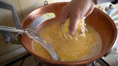 Close-up of copper cauldron with boiling water and pouring yellow cornmeal, metal whisk stirring porridge, preparation of italian traditional dish called polent. Homemade cooking of maize porridge