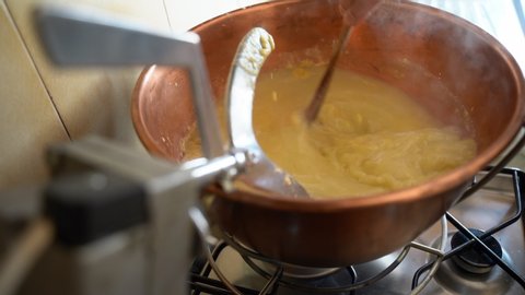 Man preparing hot polenta in copper cauldron on stove fire at home, polenta is a dish of boiled yellow cornmeal, traditional italian dish and homemade rustic recipe