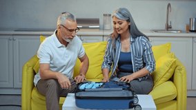 asian woman packing suitcase near senior husband