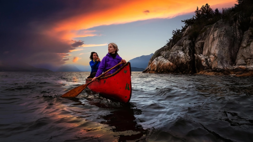 Cinemagraph Continuous Loop Animation. Couple adventurous female friends on a red canoe are paddling in the Howe Sound during a cloudy sunset. Taken in Horseshoe Bay, West Vancouver, BC, Canada.