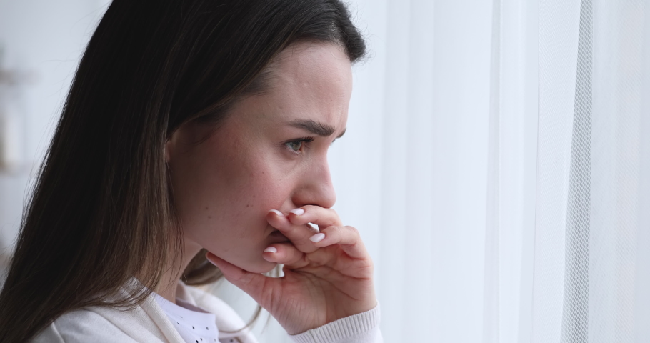 Depressed worried beautiful young woman feeling nervous, upset about problem. Anxious sad doubtful girl reflecting, looking through window and thinking of mental stress concept. Close up side face | Shutterstock HD Video #1048429240