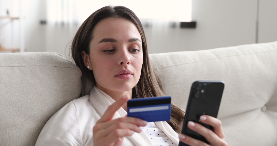 Happy young woman holding credit card using instant mobile payments at home. Smiling beautiful girl customer shopper making purchase on smart phone receiving cashback concept. E-banking app service | Shutterstock HD Video #1048429258