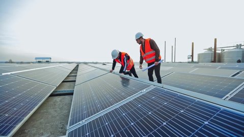 Enginneers installing new sunny batteries. Two workers in a uniform and hardhat installing photovoltaic panels on a solar farm.