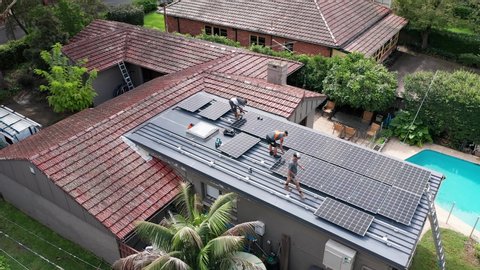Sydney, Australia - Mar 9 2020: Aerial overhead shot of tradesmen installing solar panels on a flat roof of a residential suburban home with a pool on a sunny day.