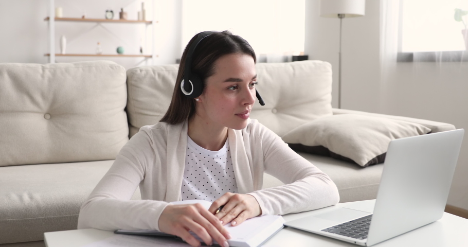 Young girl student wearing wireless headset e learning by web cam chat at home. Millennial woman video conference calling on laptop computer making notes talking by webcam. Distance education concept Royalty-Free Stock Footage #1048445902