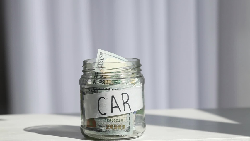 Male hand puts 100 dollars in a glass jar with the text car. Concept of saving money. Royalty-Free Stock Footage #1048467046