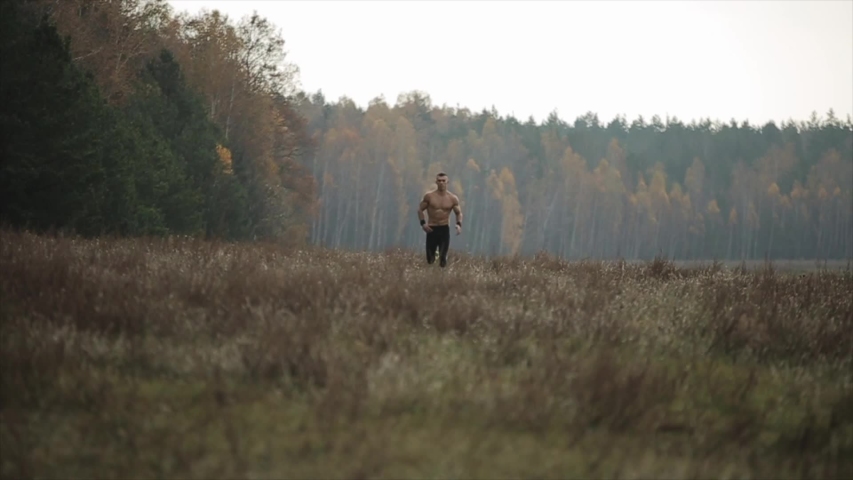 Muscular man with naked torso running across the field. Front view