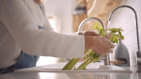 Stock video of a middle aged woman cleaning vegetables at the tap in the kitchen. She is unrecognizable.