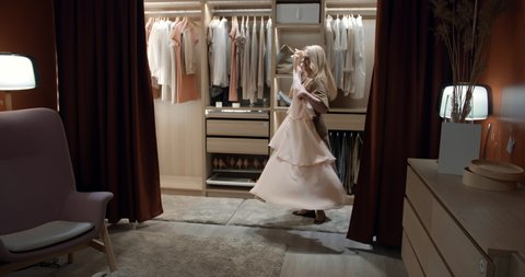 Senior elegant lady trying on dress and dancing choosing evening outfit in modern walk-in closet at home. Aged woman thinking what to wear in walk-in closet