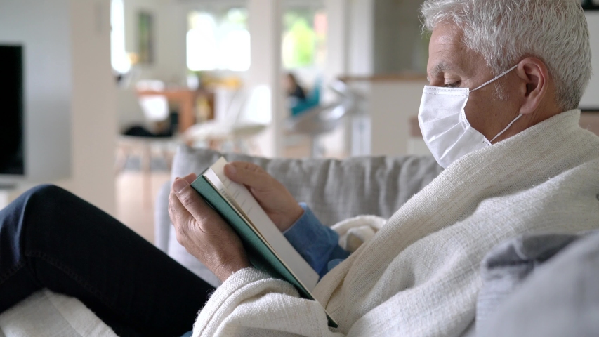Senior man at home being sick, reading book in sofa
