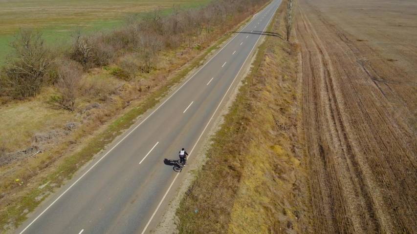 Cheerful active tourist riding his mountain bicycles up scenic rural road with bag behind . Active healthy lifestyle