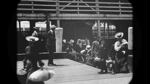 CIRCA 1903 - European immigrants arrive at Ellis Island by ship and disembark on the dock.