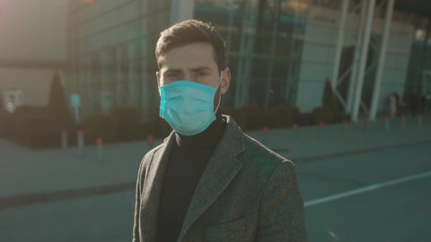 Portrait man wearing Protective Face Mask look at camera COVID-19 coronavirus infection near airport pandemic disease virus male tourist epidemic air health illness slow motion